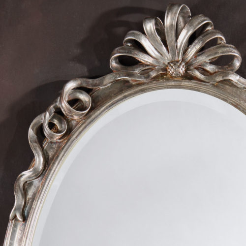 Oval Neoclassic style carved wood wall mirror with ribbon motif. This wall mirror has antique silver leaf finish and beveled glass. hand-crafted in Italy.