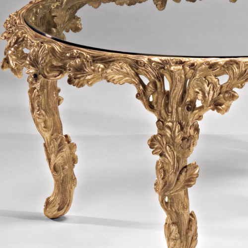 Oval carved wood coffee table with leaf motif. Carved coffee table has antiqued gold leaf finish and glass top. This carved wood table is hand-made in Italy